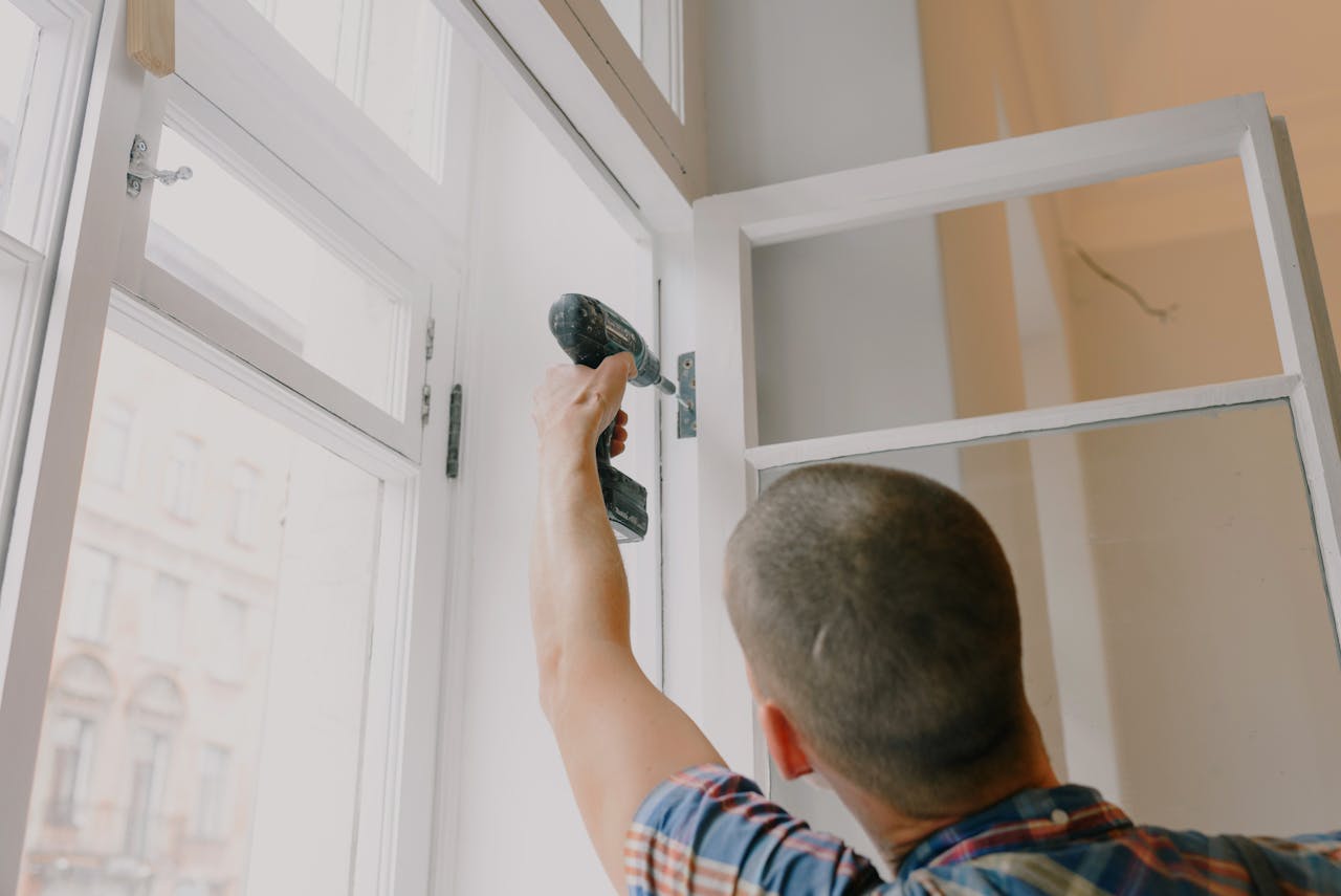 services-01 A handyman works with a drill installing window hinges indoors.
